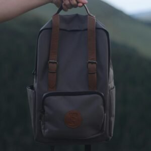 A person holding a stylish gray backpack with leather straps, set against a natural outdoor background.
