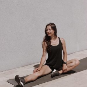 Woman performing a seated stretch outdoors on a yoga mat, enjoying a sunny day.