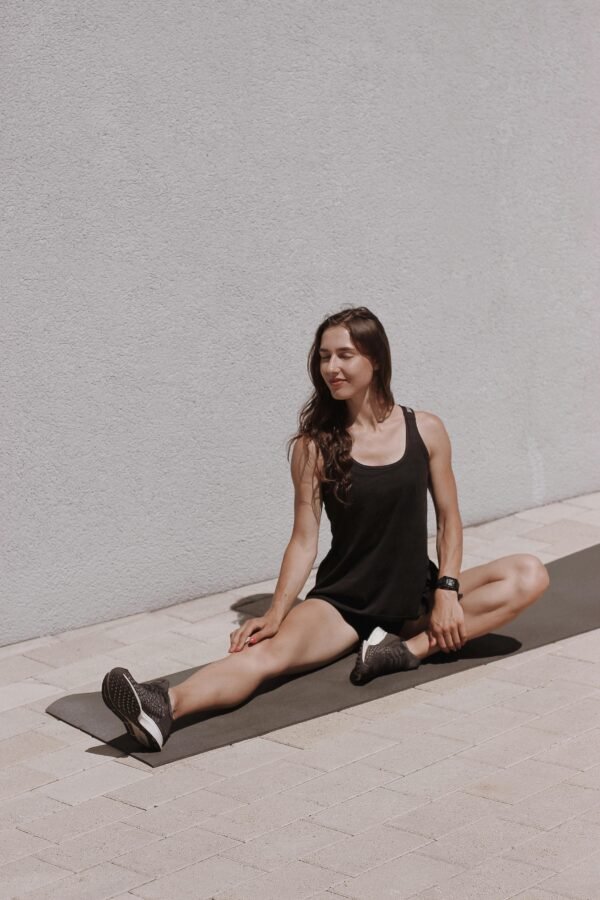 Woman performing a seated stretch outdoors on a yoga mat, enjoying a sunny day.