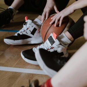 A close-up of athletes resting with a basketball, showcasing sneakers on a wooden court floor.
