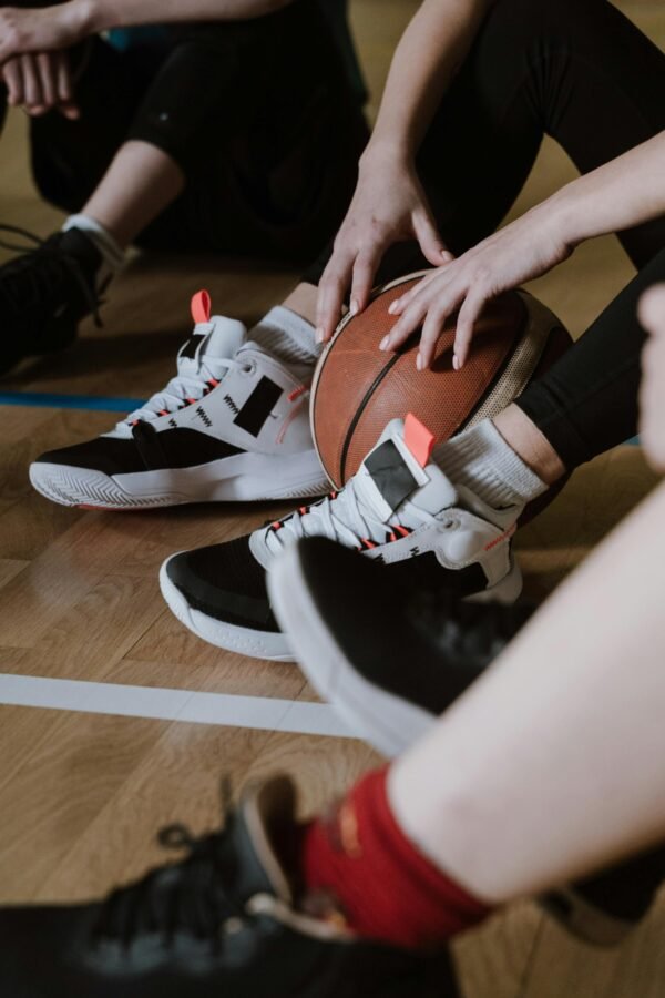 A close-up of athletes resting with a basketball, showcasing sneakers on a wooden court floor.